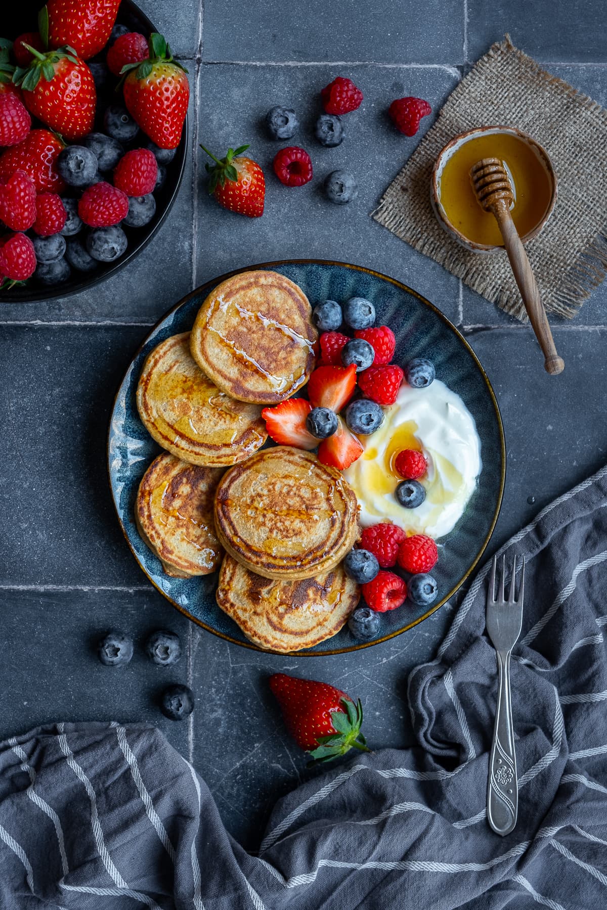 Overhead shot of 3 Ingredient Banana Oat Egg Pancakes on a plate next to berries, honey and yogurt