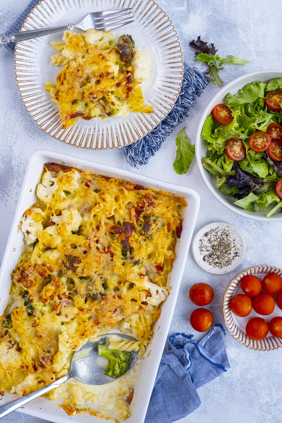 Overhead shot of Cauliflower, Broccoli and Bacon Pasta Bake in an oven dish with salad.