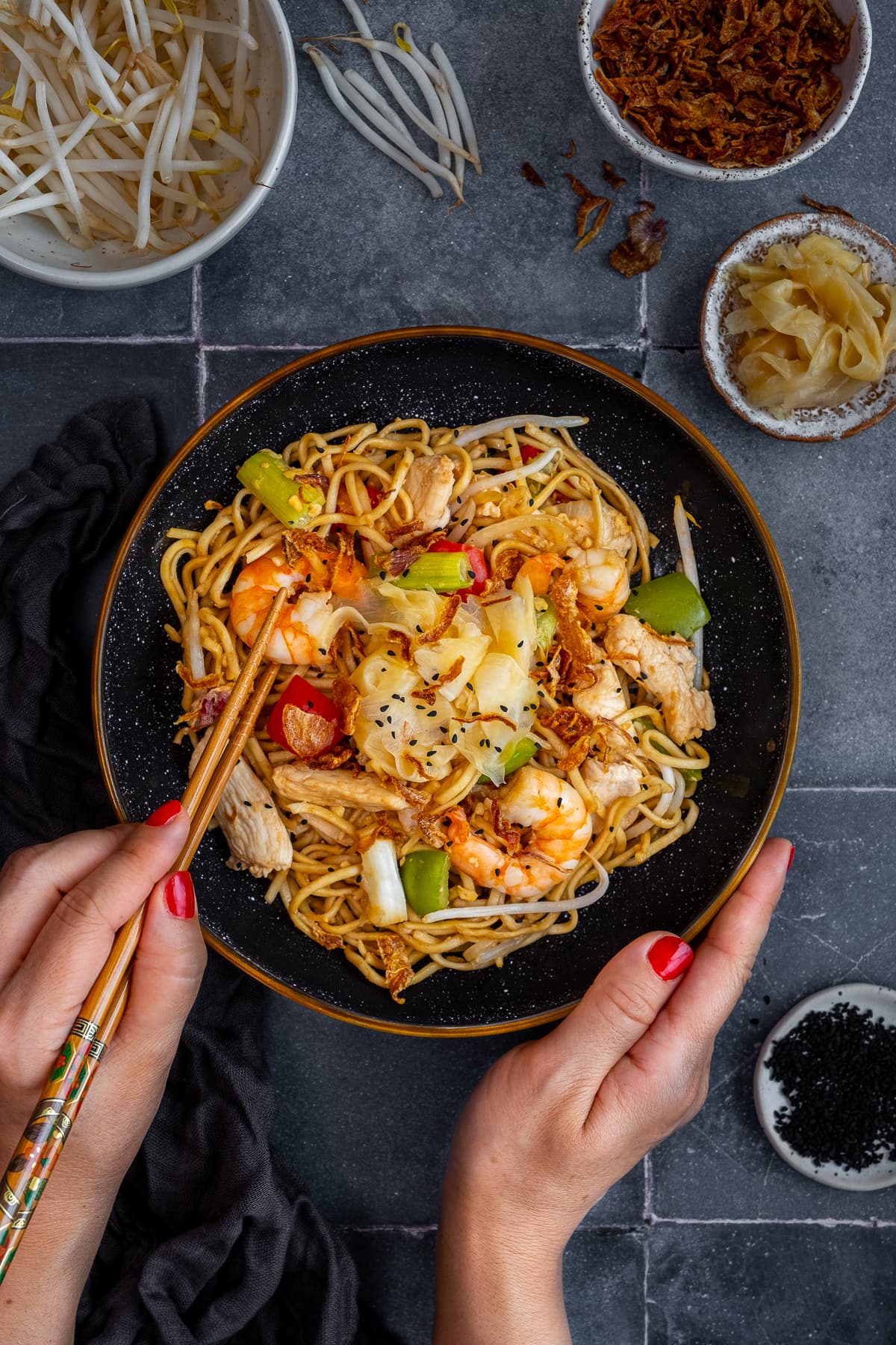 Overhead shot of Chicken and Prawn Yaki Soba with chopsticks held by a woman's hands