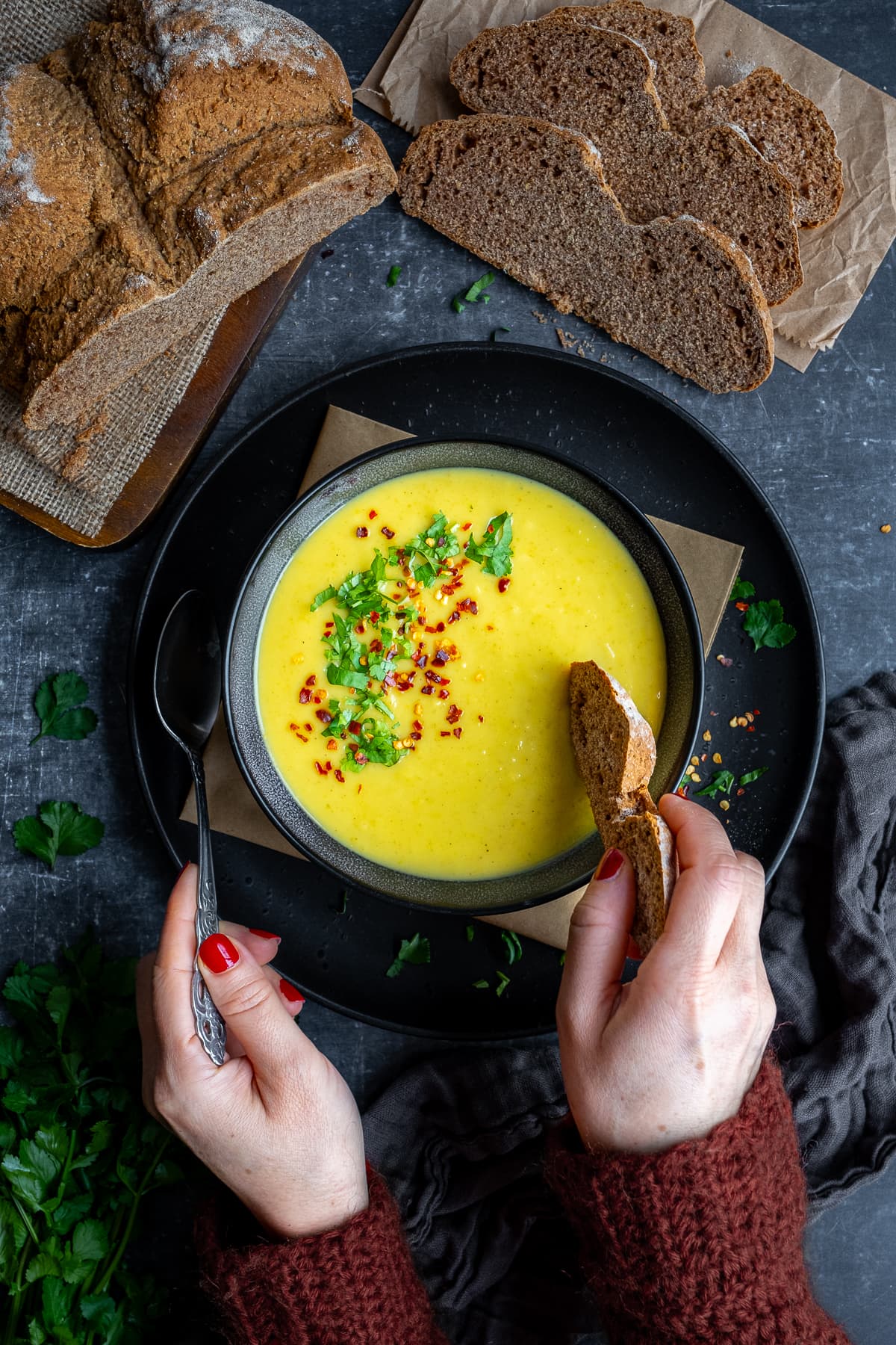 A bowl of Curried Parsnip Soup. A woman's hands holding a spoon, taking a spoonful of soup.