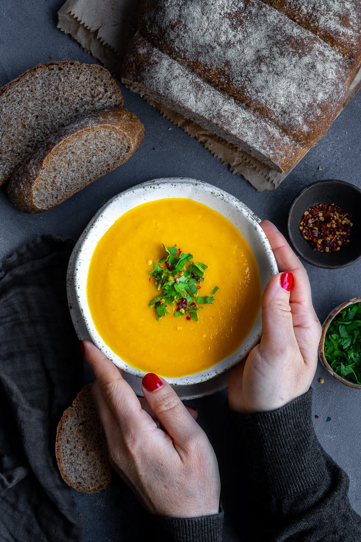 Overhead shot of 1 bowl of Easy Carrot and Butternut Squash Soup. A woman's hands are holding the bowl.