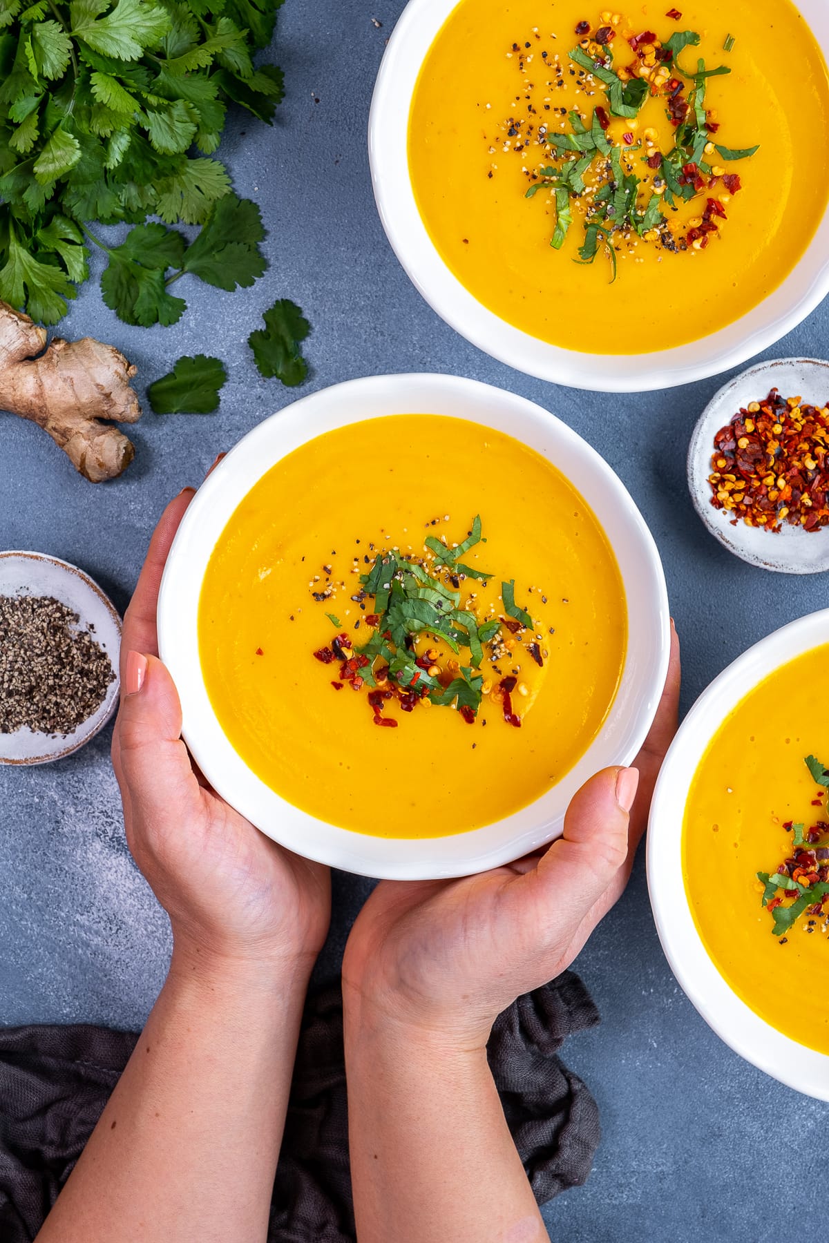 Overhead shot of 3 bowls of Easy Carrot and Parsnip Soup, one is being held up to the camera