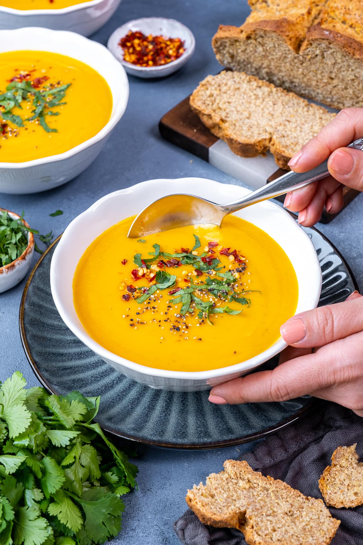 Easy Carrot and Parsnip Soup in a bowl, with a woman's hand holding a spoon in the soup