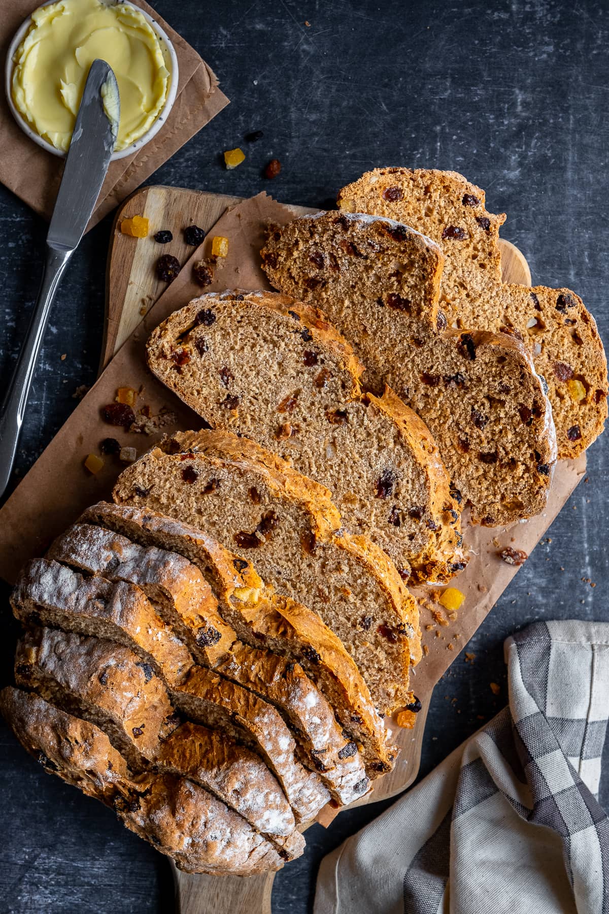 Overhead shot of a sliced loaf of Easy Fruit Soda Bread on a wooden board with butter.