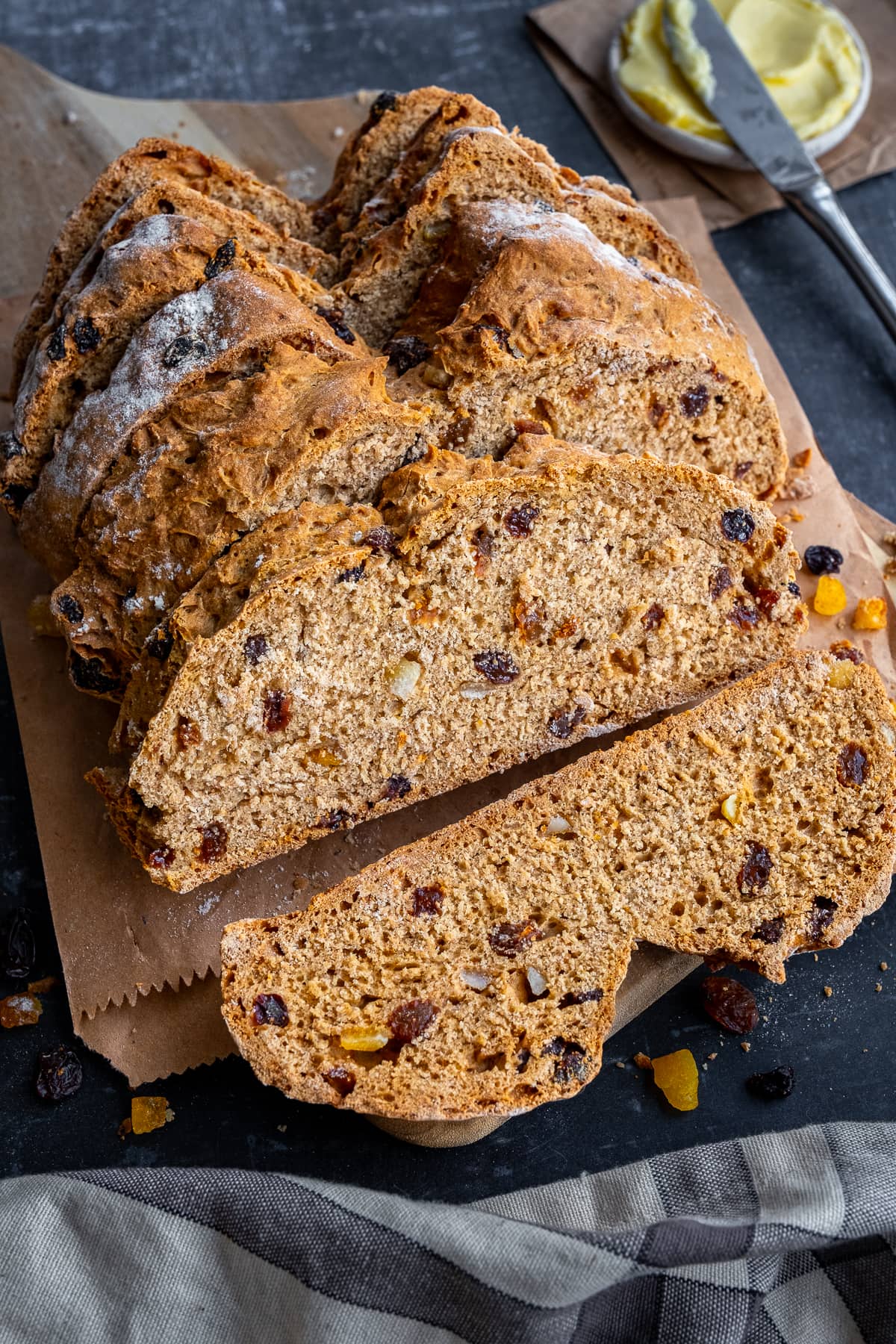 Sliced loaf of Easy Fruit Soda Bread on a wooden board with a pot of butter in the background.