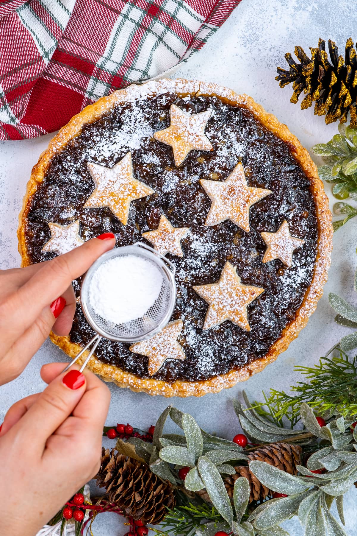 Woman's hand sprinkling icing sugar in a small sieve over Easy Mincemeat Tart