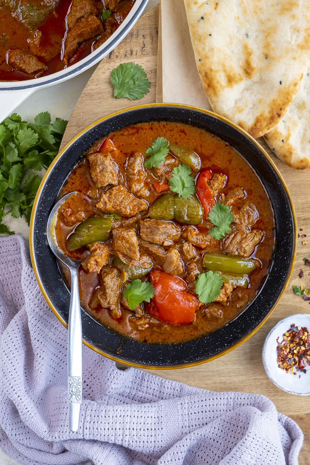 Overhead shot of Easy Peasy Beef Curry on a plate surrounded by naans and coriander