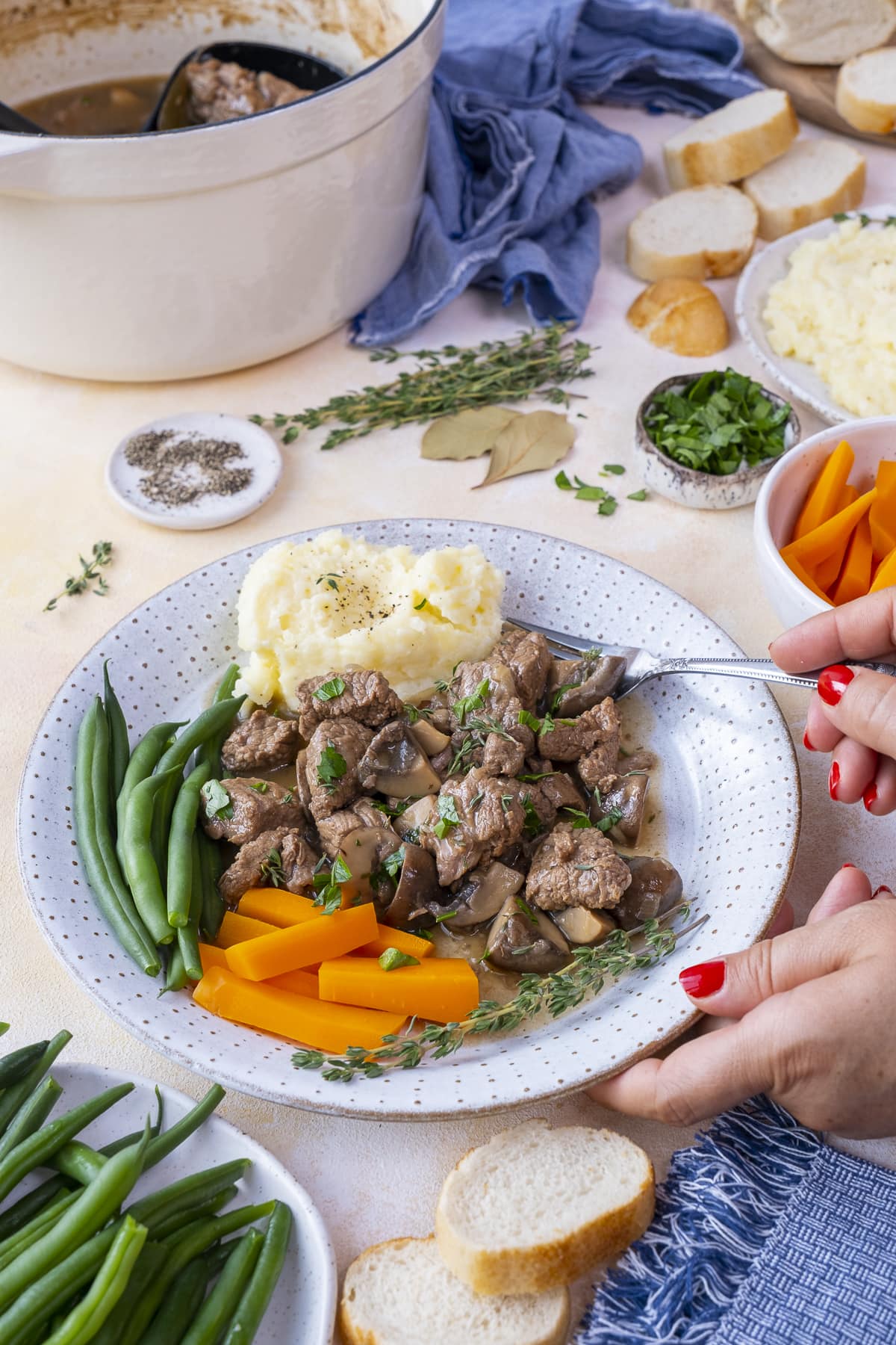 Easy Peasy Beef Stew on a plate with mashed potatoes, carrots and green beans. A ladies hand is holding a fork, looking like she's about to take a mouthful.