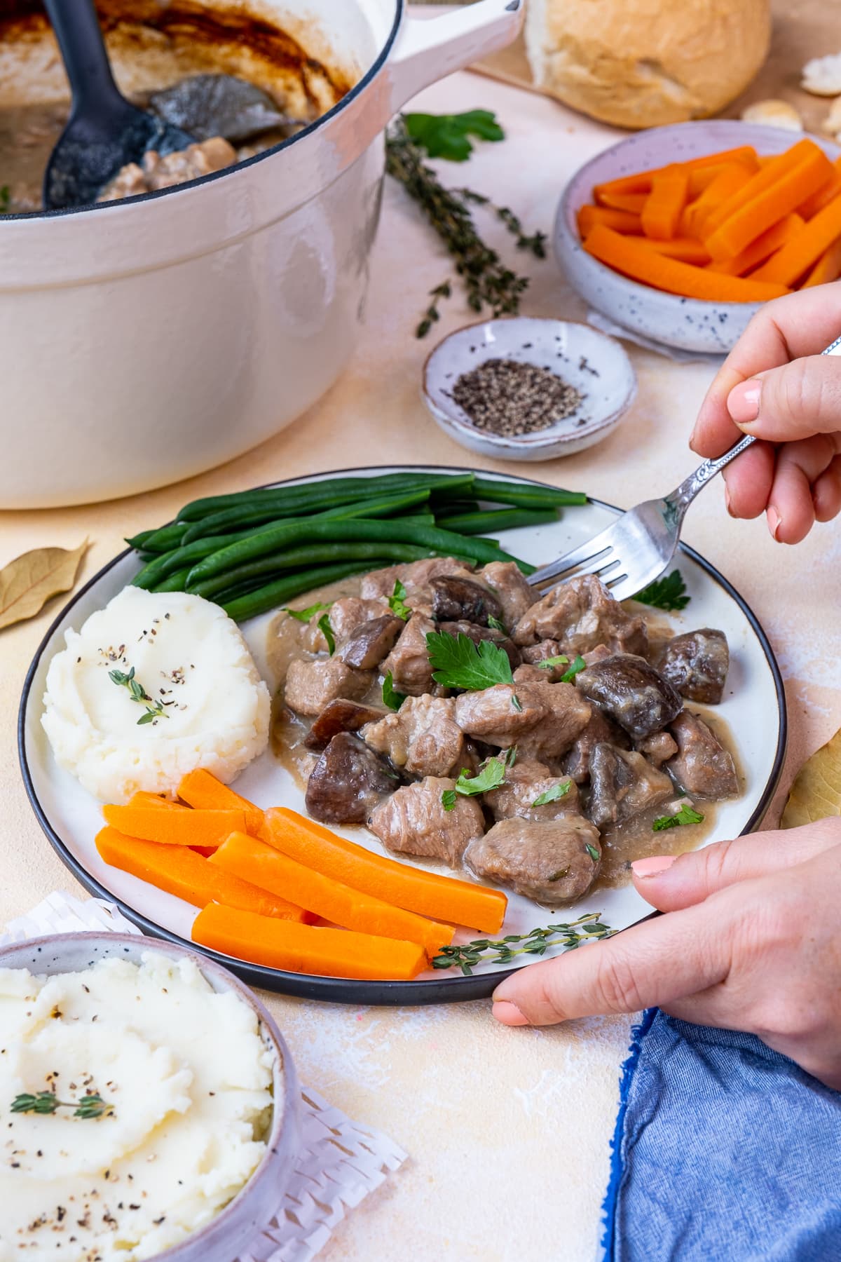 Easy Peasy Lamb Stew on a plate. Woman's hand holding a fork and taking a forkful of the stew