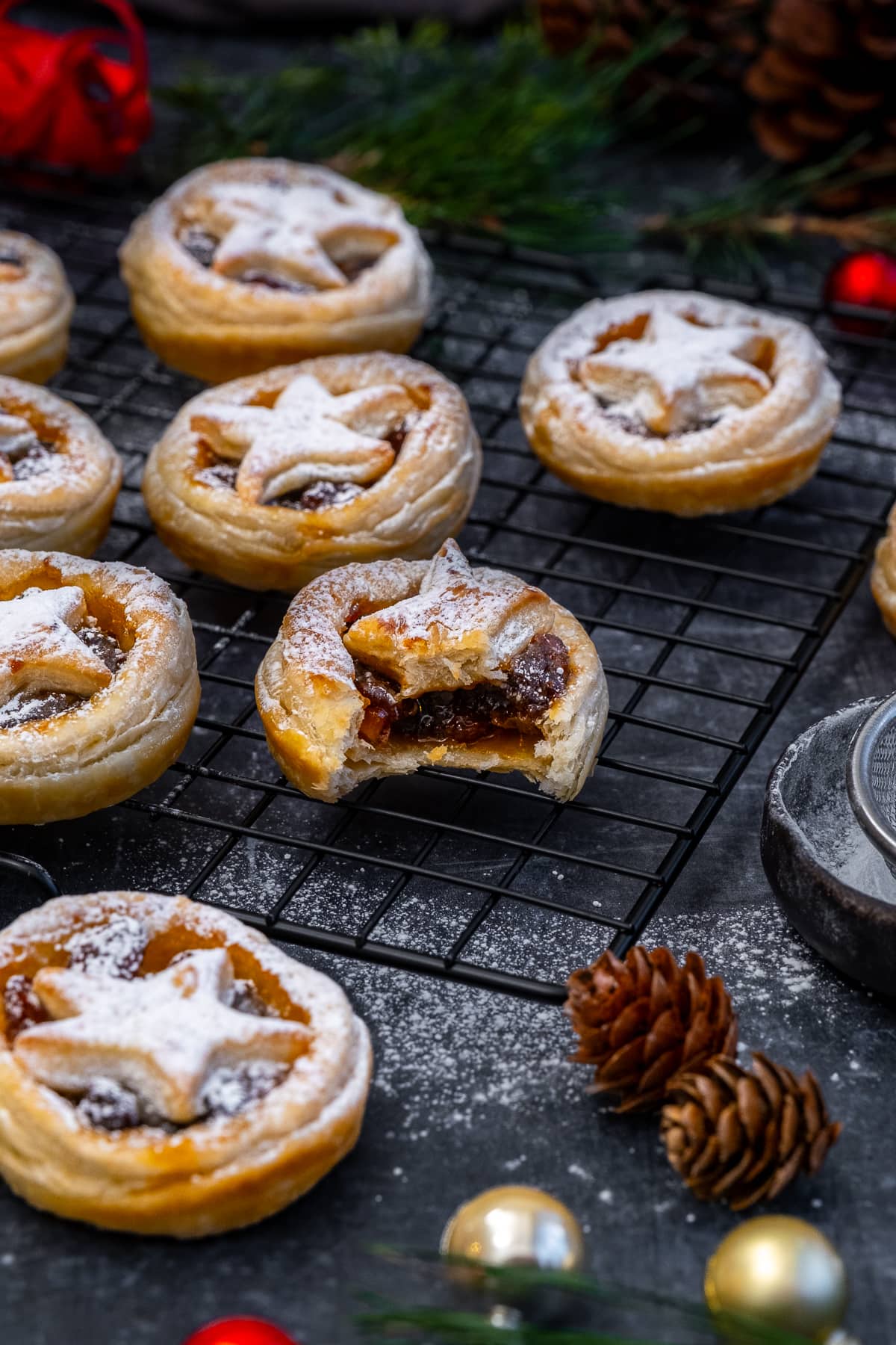 Easy Puff Pastry Mince Pies on a cooling rack -one has a bite taken out of it.