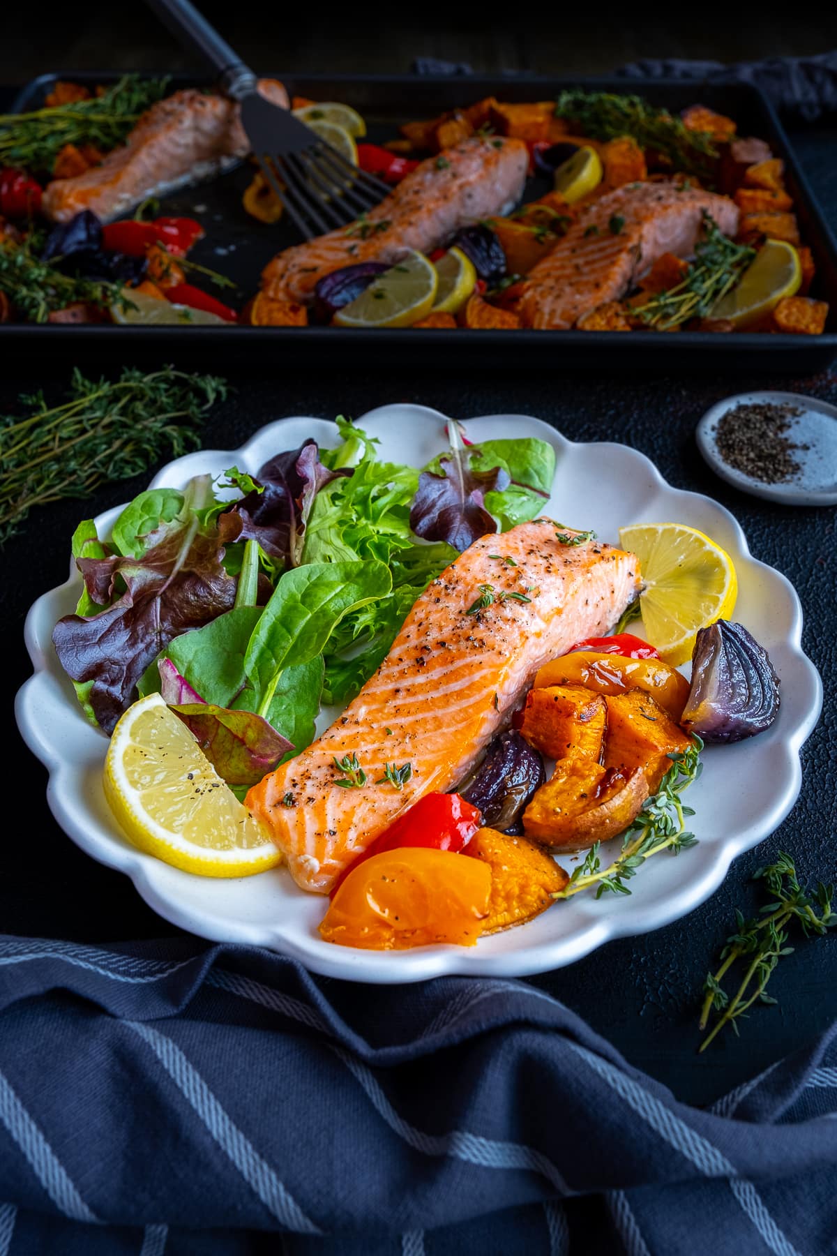 One cooked salmon fillet on a plate with roasted vegetable and salad leaves