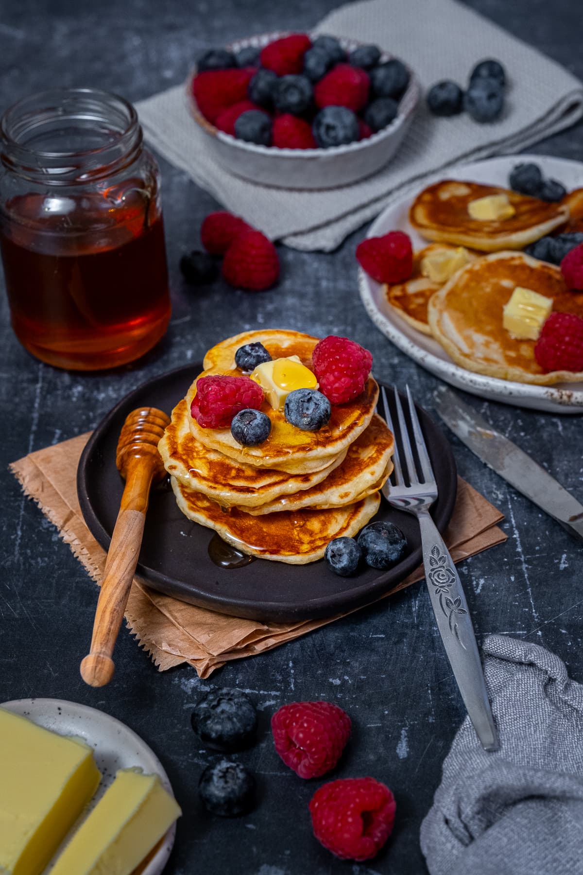 A stack of scotch pancakes topped with berries, butter and honey.