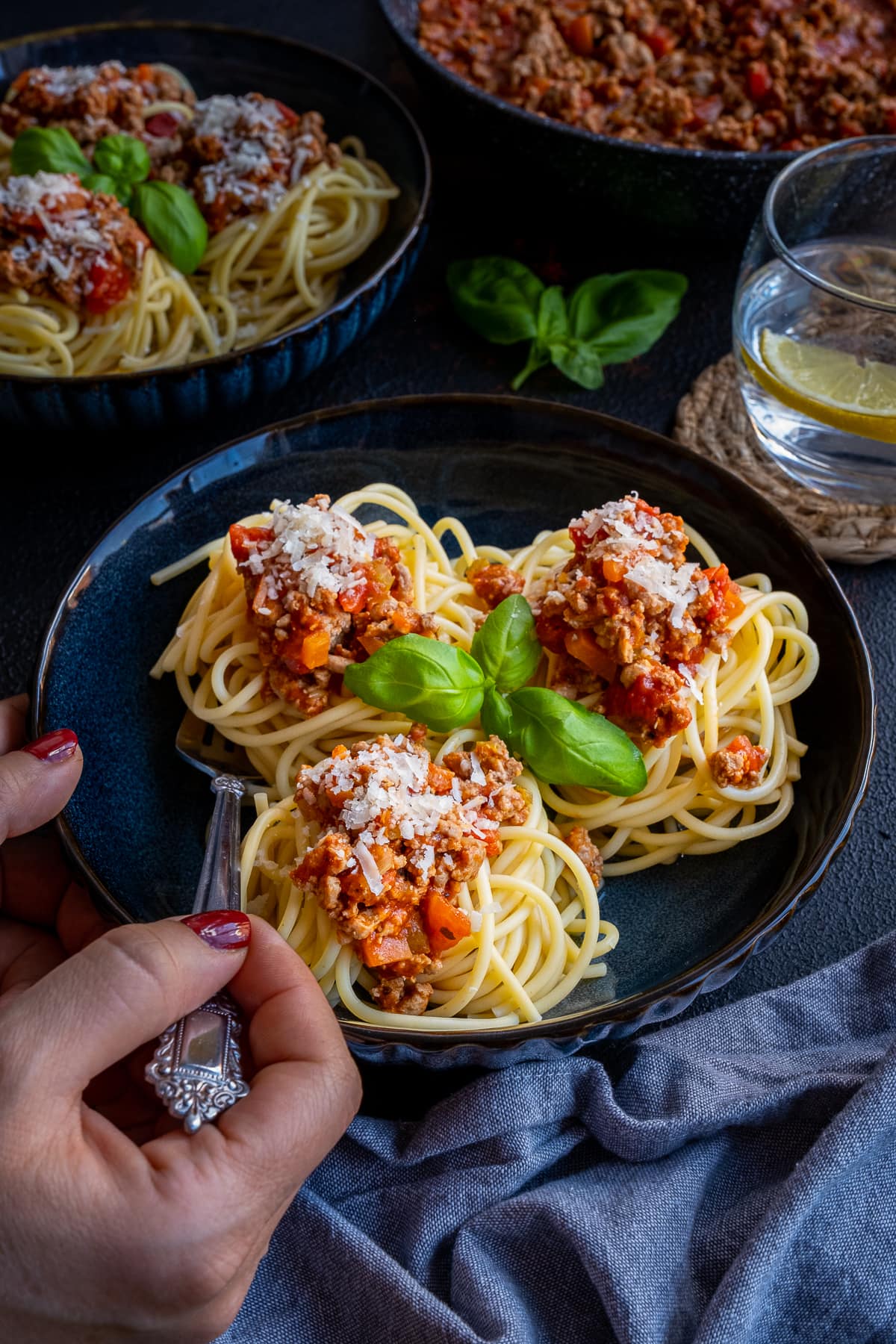 Easy Turkey Mince Bolognese on a plate. A woman's hand is holding a fork which is about to take some of the bolognese.