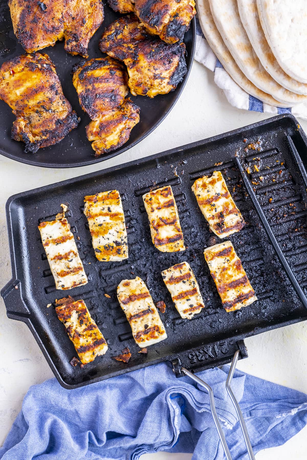 8 halloumi slices on a griddle pan (with char lines), next to a board with griddled chicken