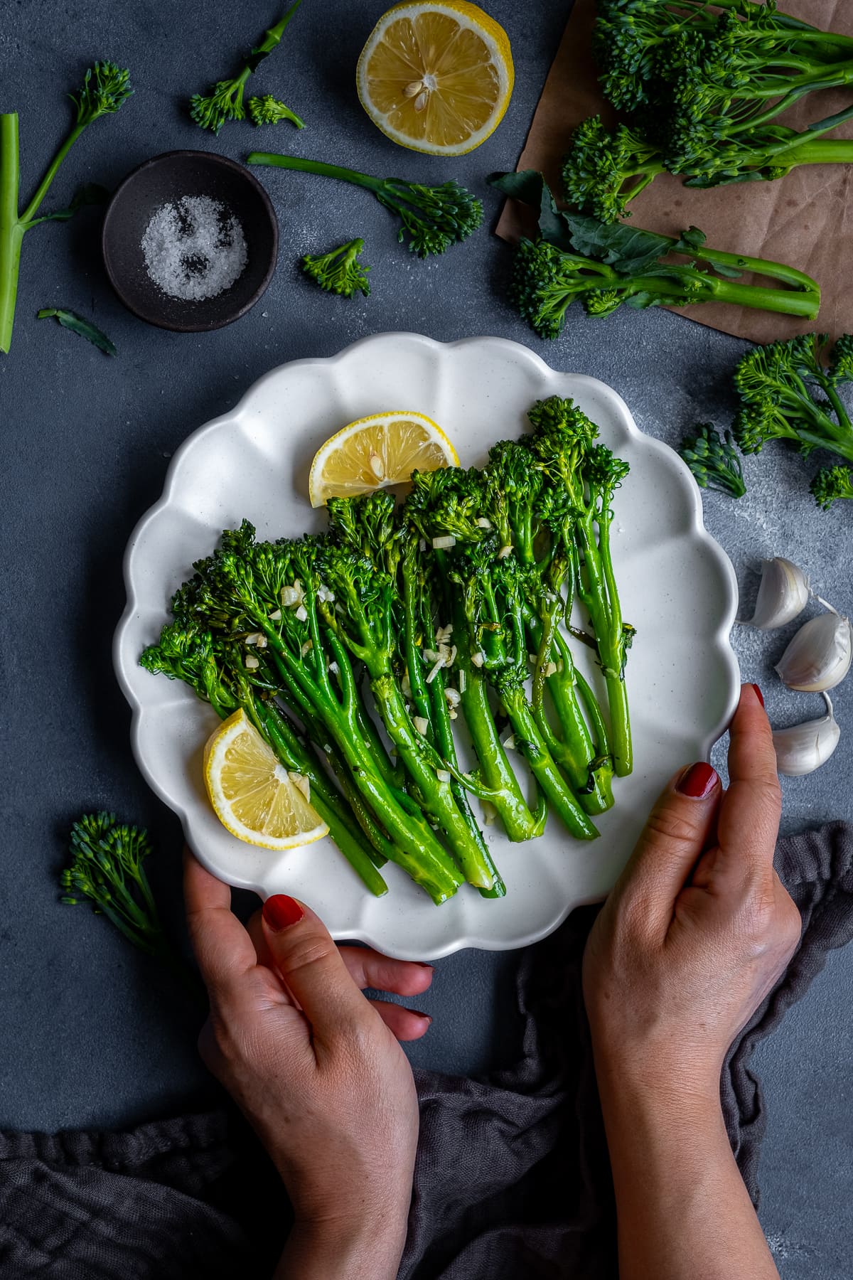 Overhead shot of Homemade Nando’s Lemon and Garlic Broccoli on a white plate being held by a woman's hands