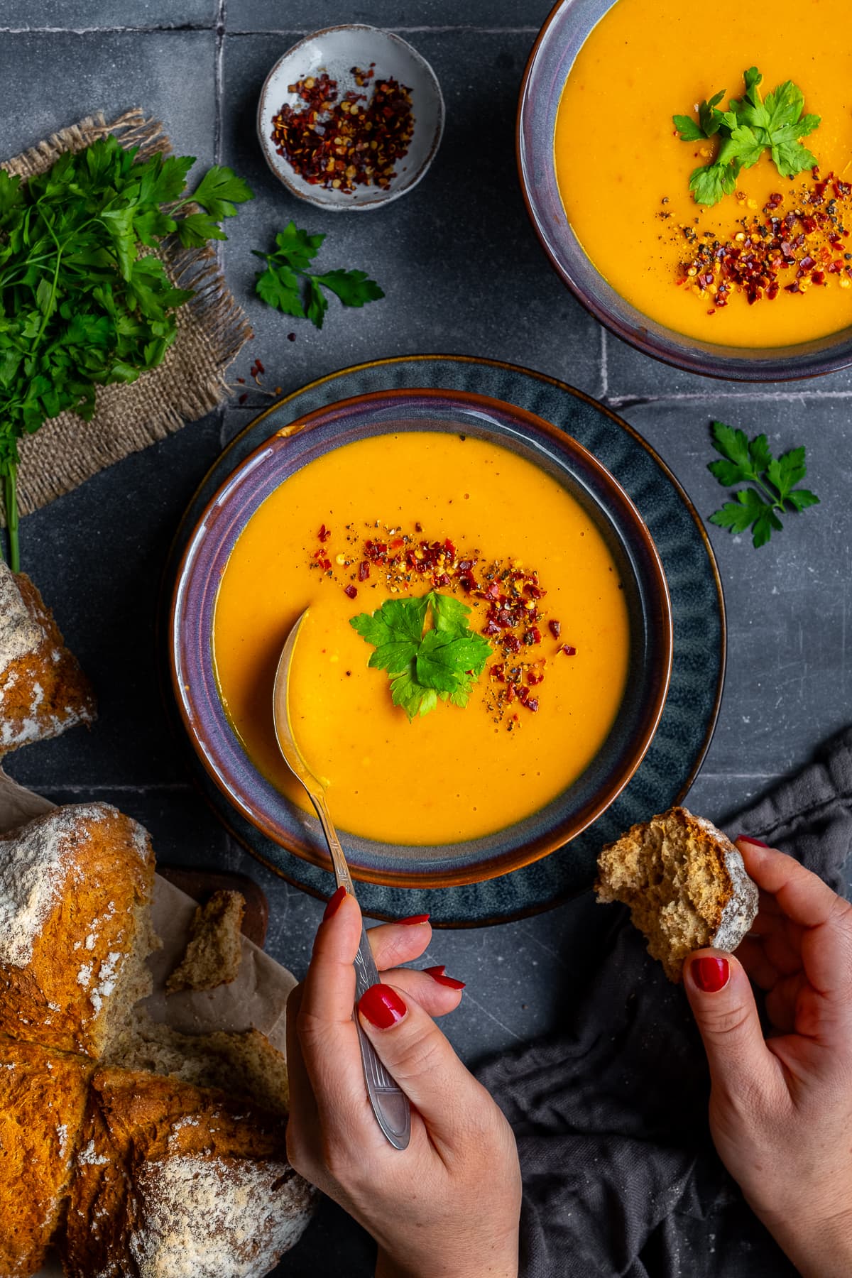 Overhead shot of Immune System Booster Soup in a bowl. A woman's hands are holding a spoon and some soda bread.