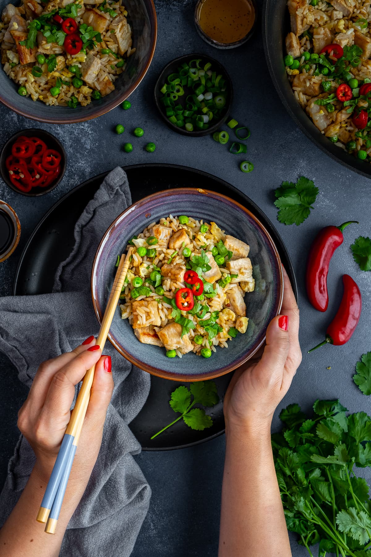 Overhead shot of Leftover Pork Fried Rice in a bowl, with chopsticks held by a woman's hands