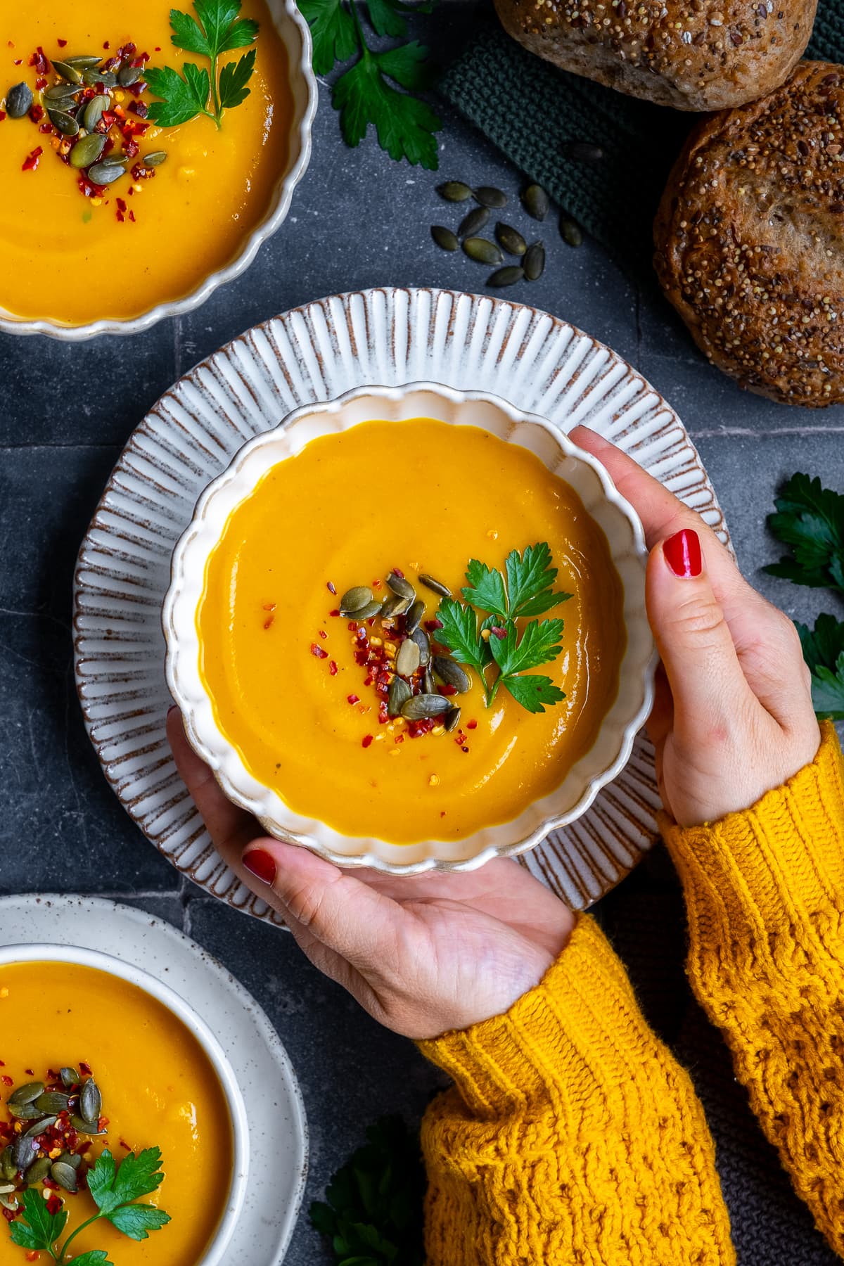 Overhead shot of 3 bowls of Pumpkin and Sweet Potato Soup. A woman's hand is holding the middle bowl.