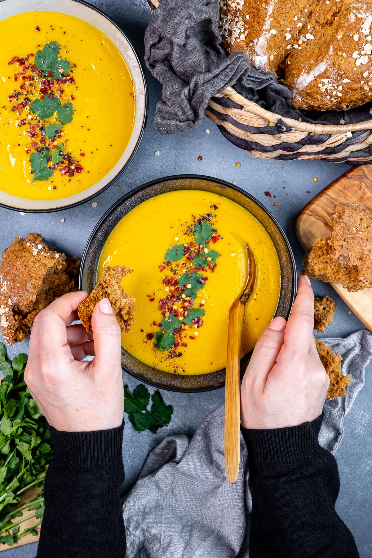 Overhead shot of someone dipping soda bread in a bowlful of Spiced Carrot and Lentil Soup