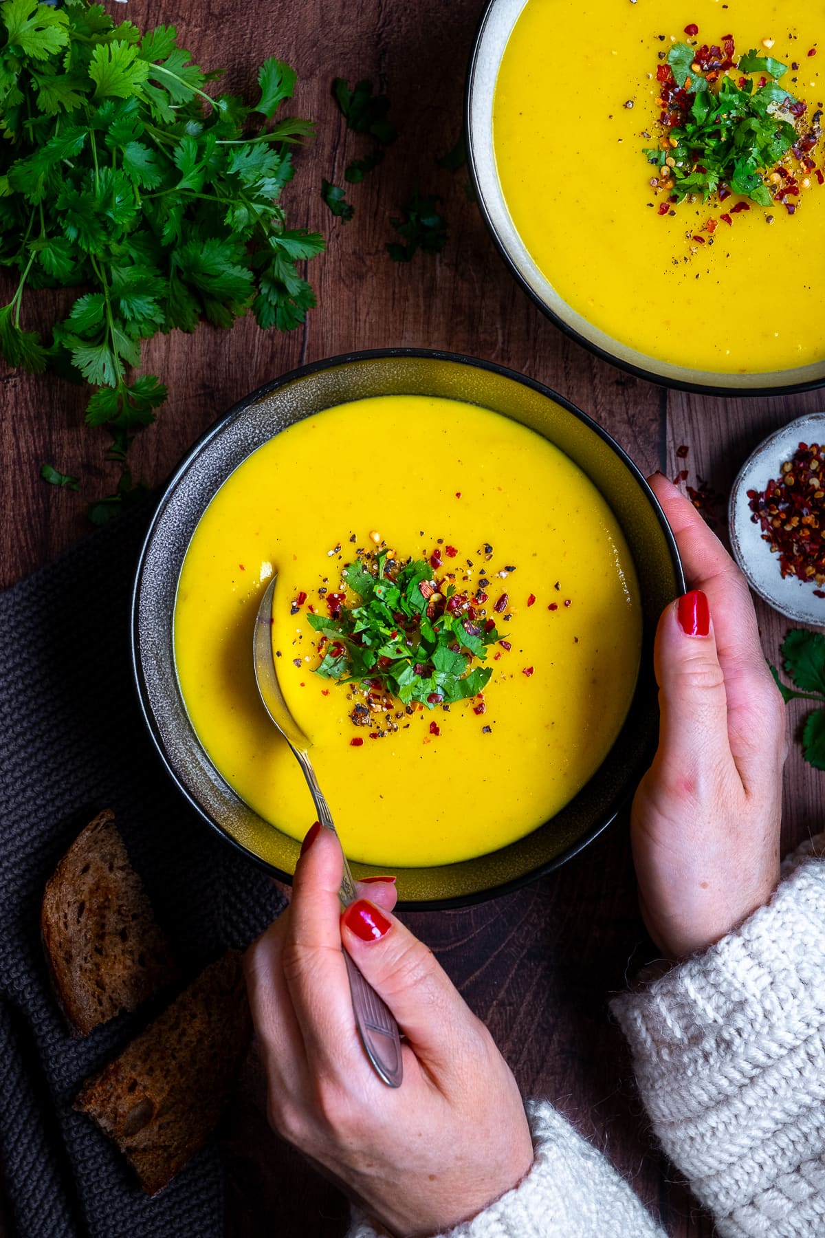 2 bowls of Spicy Parsnip Soup. Woman's hands holding the bowl and a spoon.