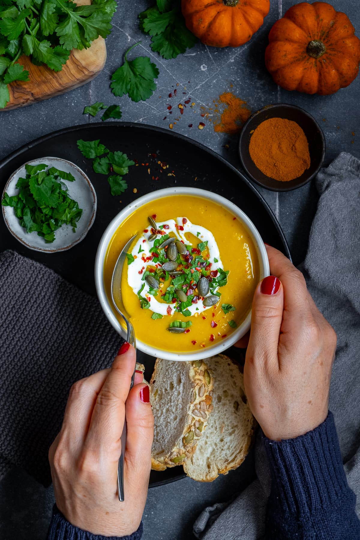 Overhead shot of a woman's hands taking a spoonful of Spicy Pumpkin Soup