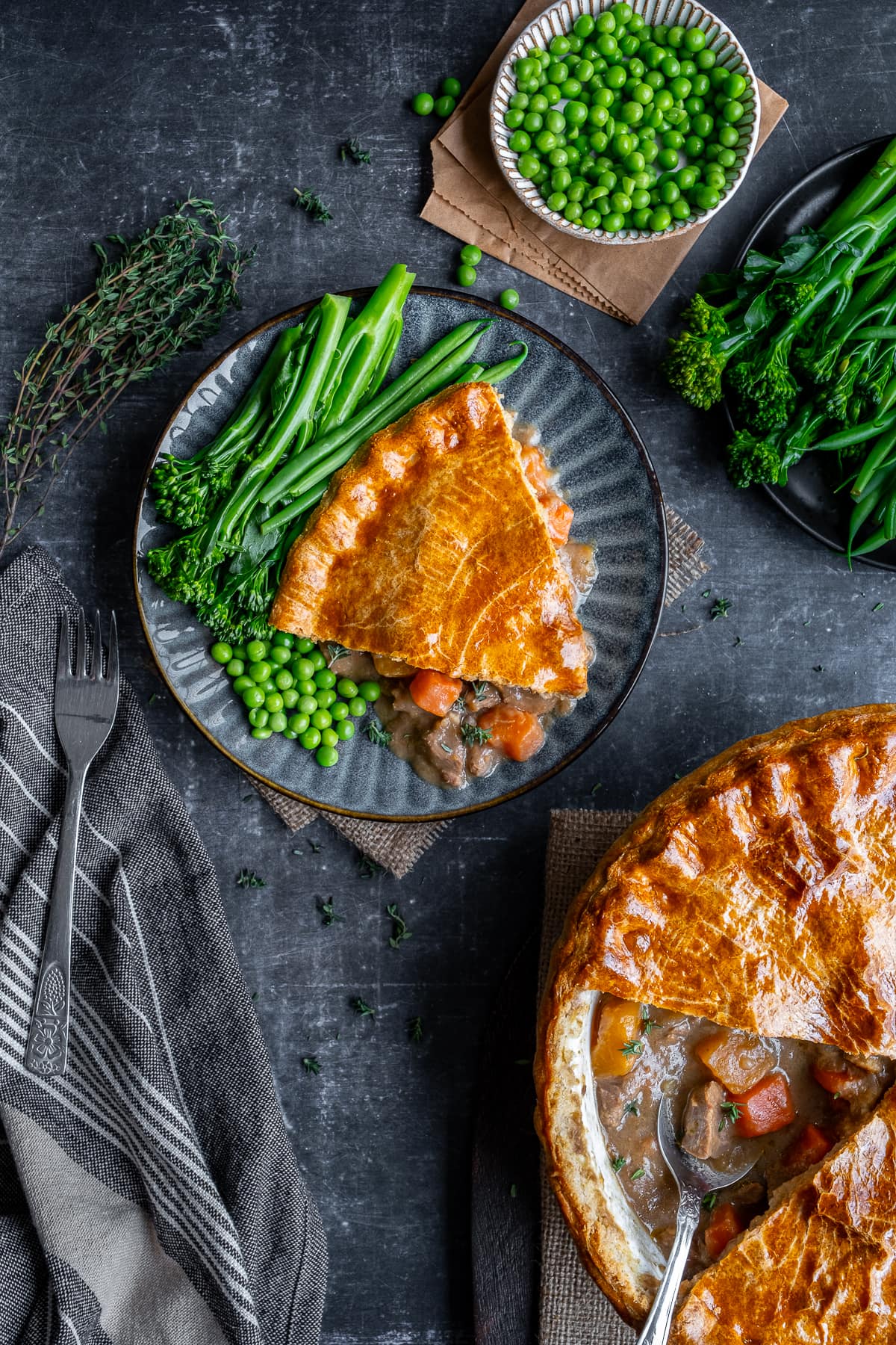 One portion of Suet Crust Steak Pie on a plate with broccoli and peas.