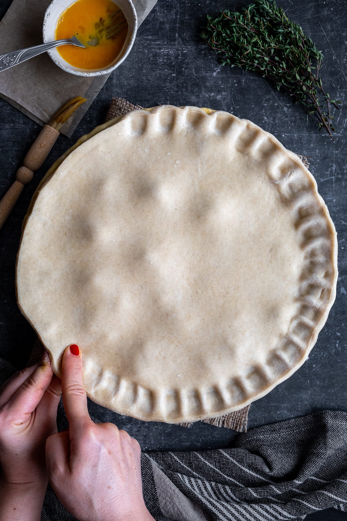 Uncooked suet crust pastry on top of the pie filling. A woman's hands are crimping the edges of the pie.